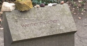 gravestone with pebbles on top and the engraved text "weitermachen!"